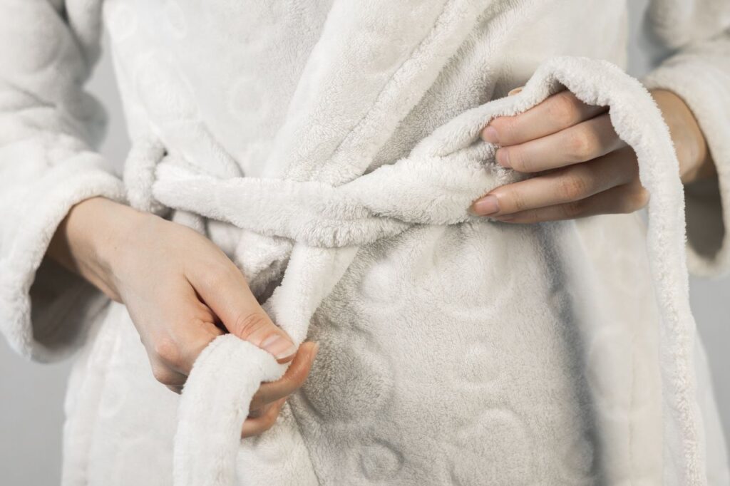 Mains d'une femme nouant la ceinture d'un peignoir blanc